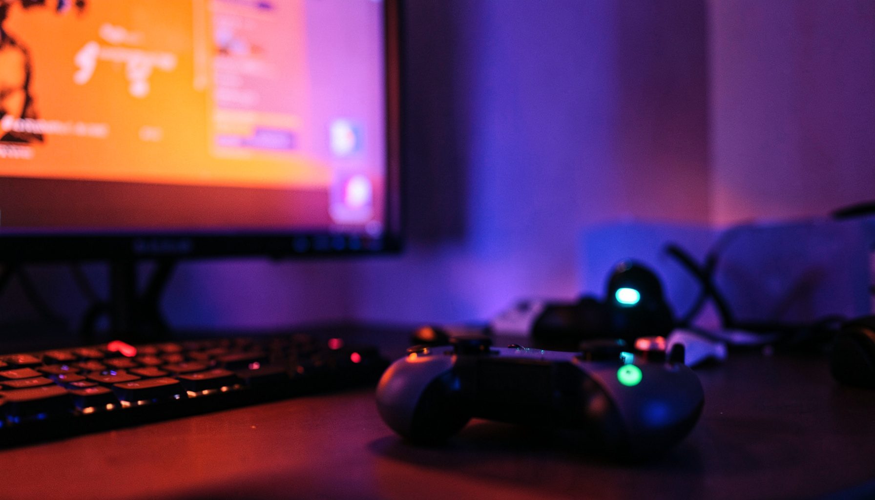 A gaming controller resting on a desk beside a glowing monitor, deep purple and blue ambient light